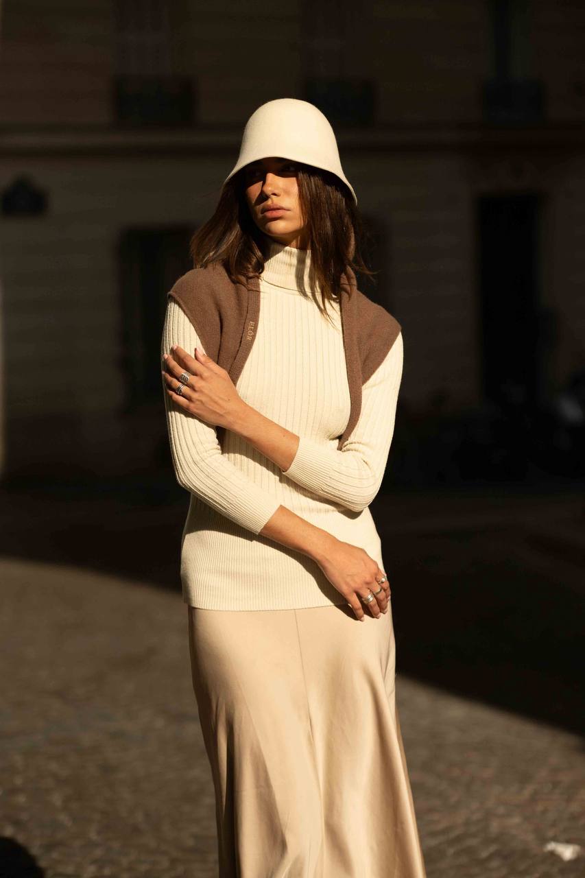 Modelo con cloché de lana marfil, suéter de cuello alto y falda de satén, en una calle de París
