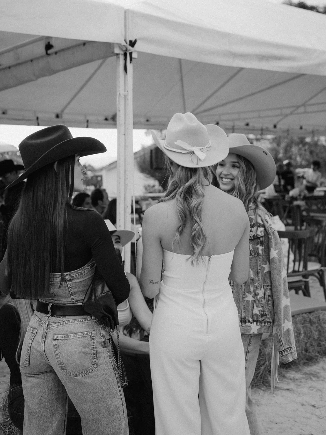 Tres invitadas con sombreros cowboy conversando bajo la carpa del evento, una de ellas con sombrero ELÓR