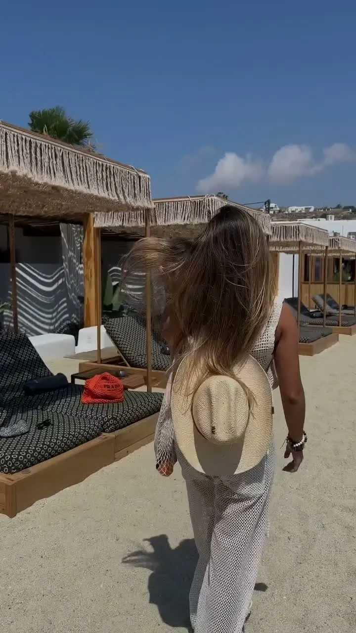 Mujer caminando entre camas de playa con un sombrero de paja en la mano