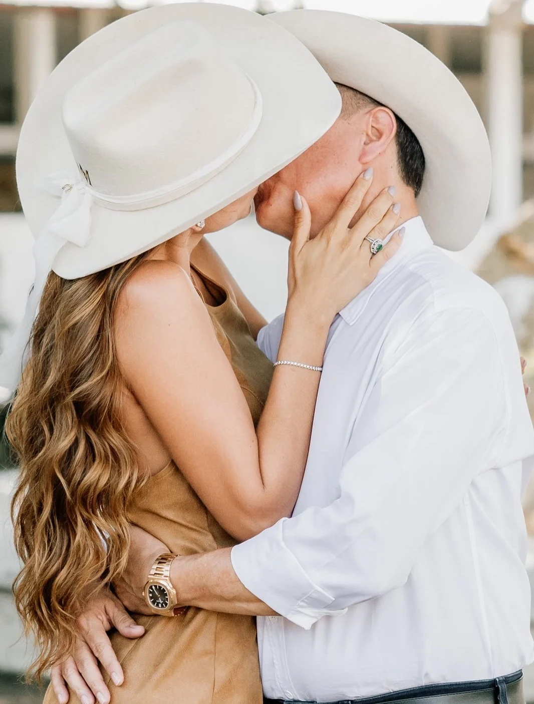 Pareja besándose bajo dos sombreros cowboy blancos el día de su boda