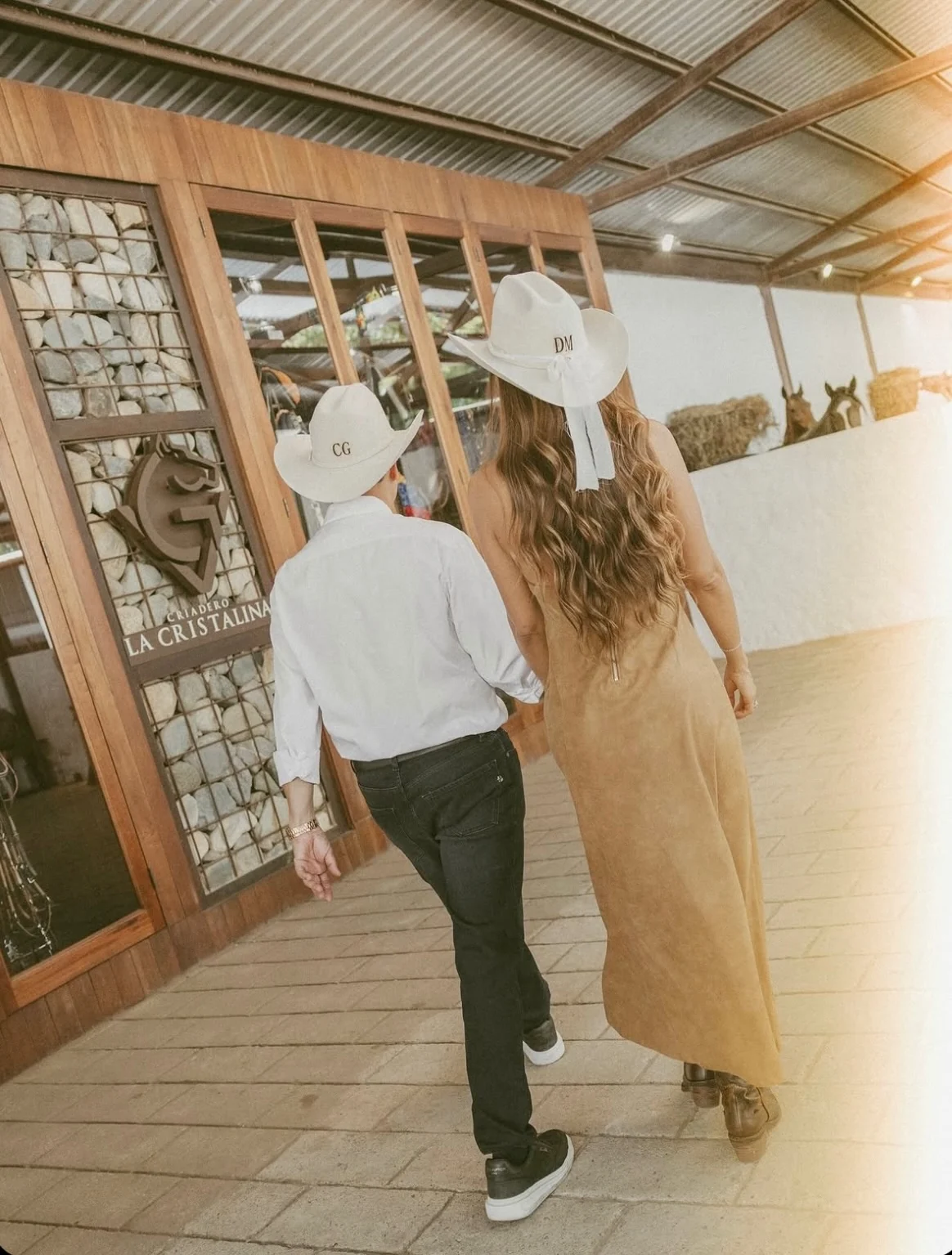 Pareja de espaldas con sombreros cowboy blancos personalizados con sus iniciales, ella con lazo de novia