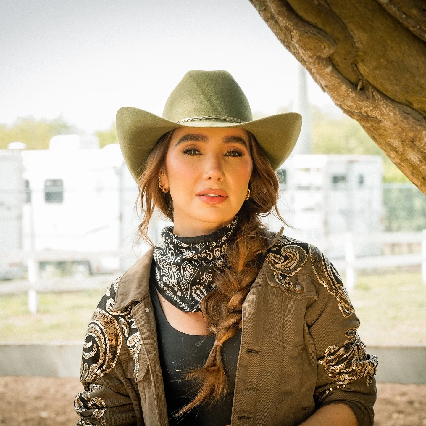 Mujer con sombrero verde oliva y bandana entre dos caballos