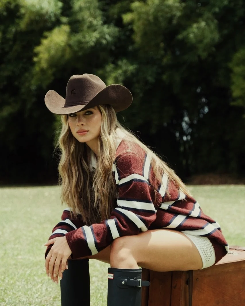 Modelo con sombrero de fieltro y suéter de rayas sentada al aire libre