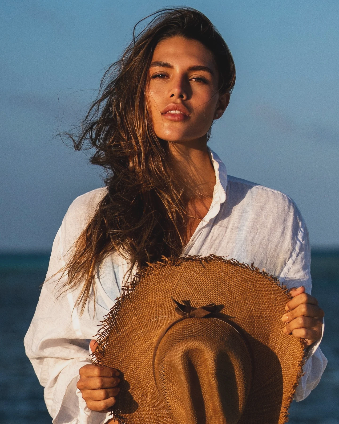Retrato en la playa con un sombrero de paja abrazado contra el pecho