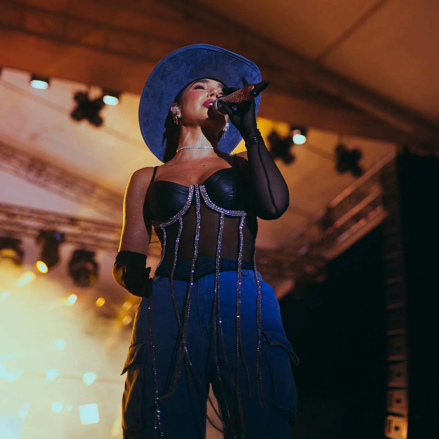 Cantante en concierto con sombrero cowboy azul bajo las luces del escenario