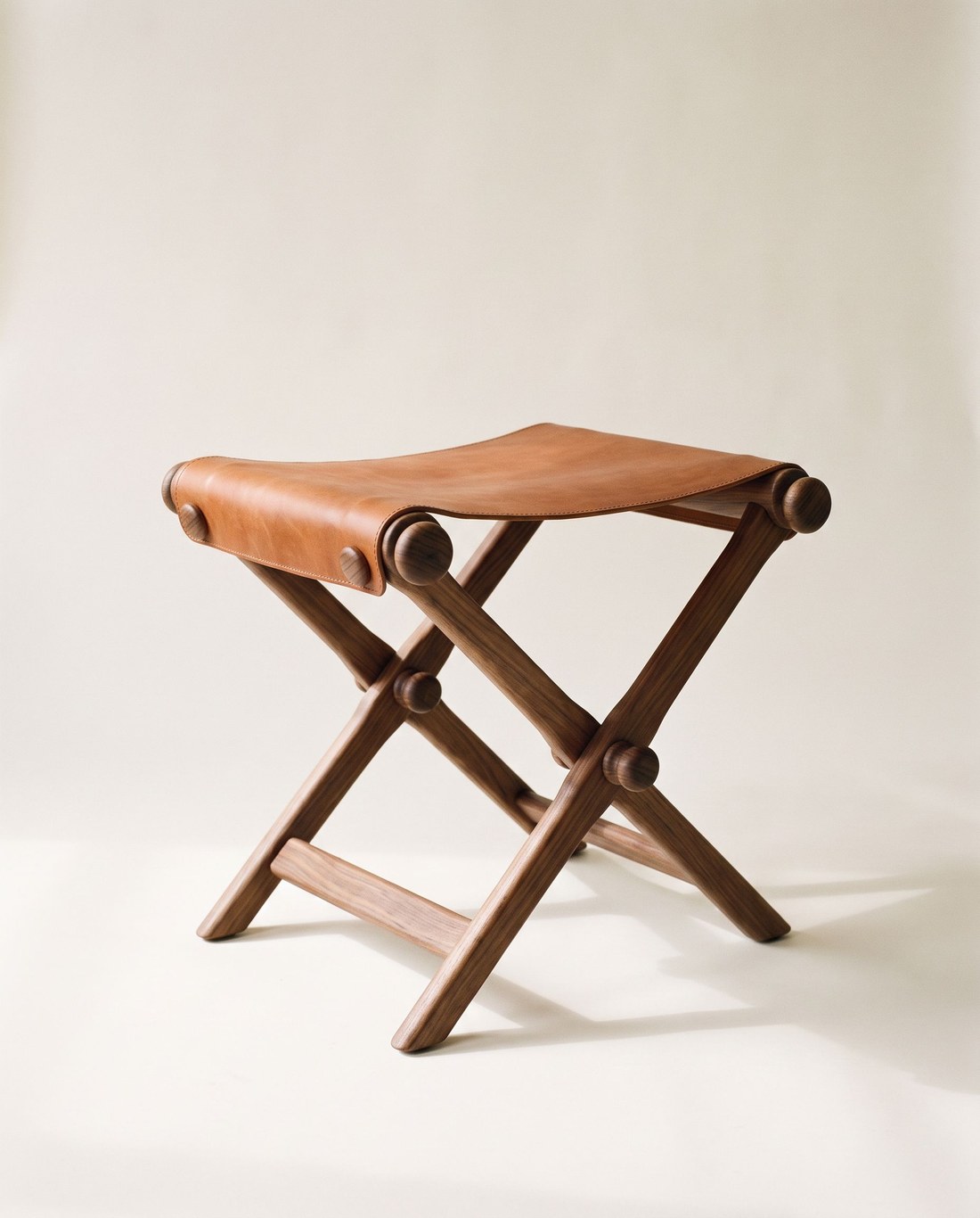 ESTRIBO, banqueta plegable de nogal con asiento de cuero de montura y botones de madera, retrato de estudio