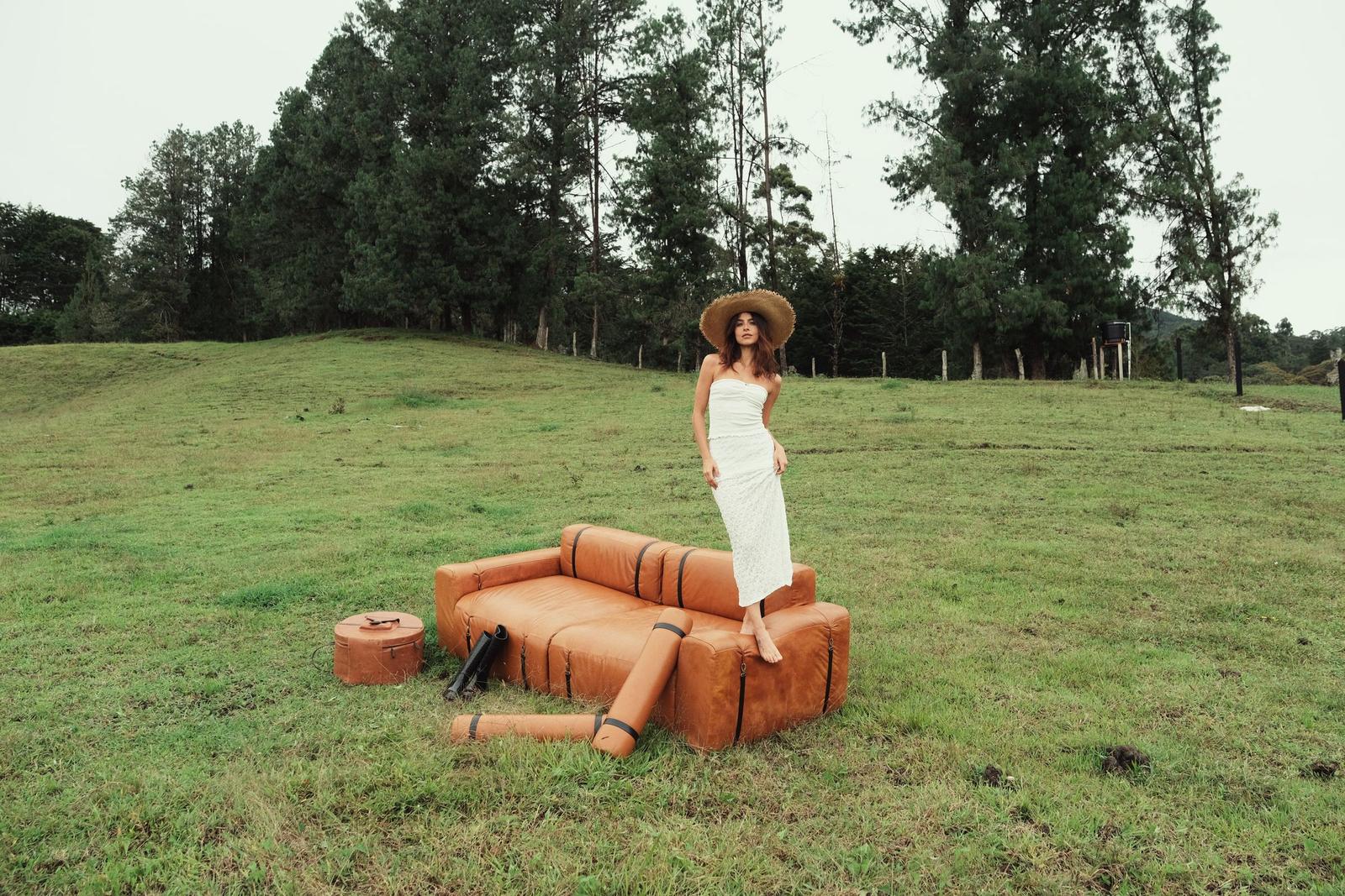 Modelo con sombrero de paja sobre un sofá ONDA MODULAR de cuero cognac, en un potrero entre pinos