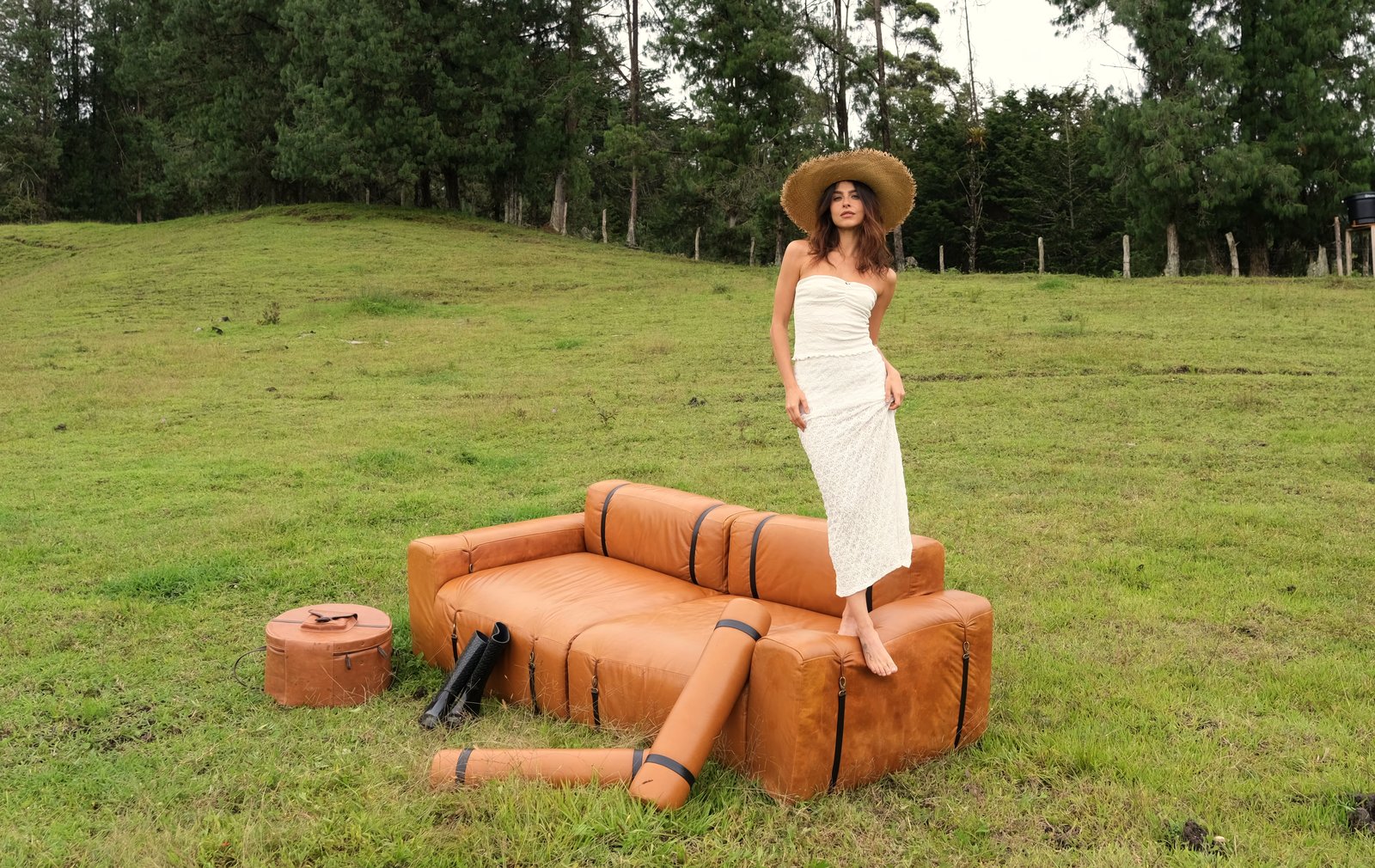Modelo con sombrero de paja sobre un sofá ONDA MODULAR de cuero cognac, en un potrero entre pinos