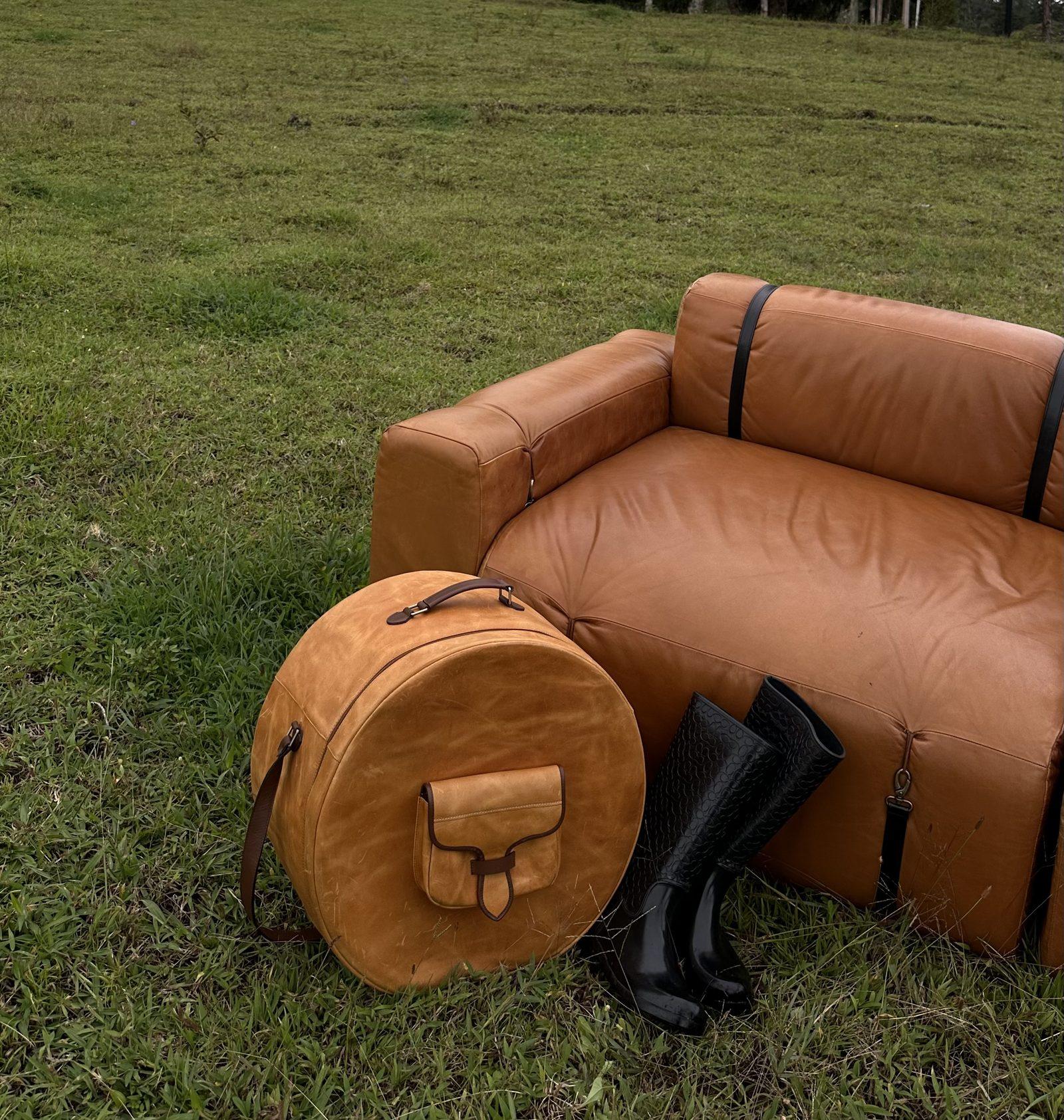 Sofá ONDA MODULAR de cuero cognac sobre el pasto, junto a una sombrerera de cuero y botas de campo