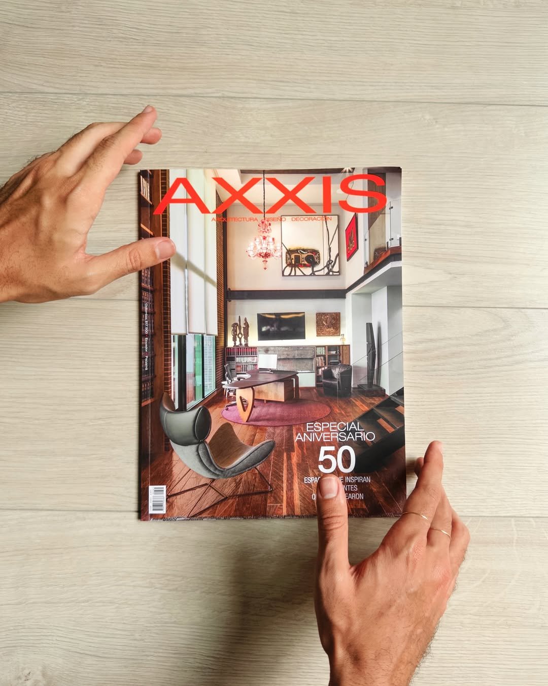 Manos sosteniendo la edición 50 aniversario de Revista Axxis sobre una mesa de madera